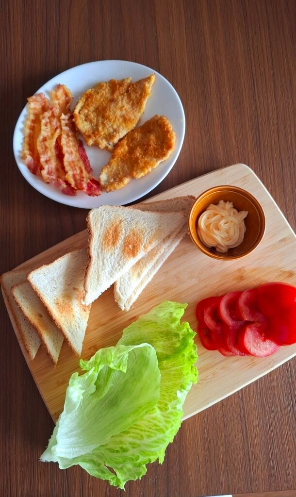 Tutti gli ingredienti per club sandwich: pane bianco cotoletta pollo insalata pomodoro maionese bacon