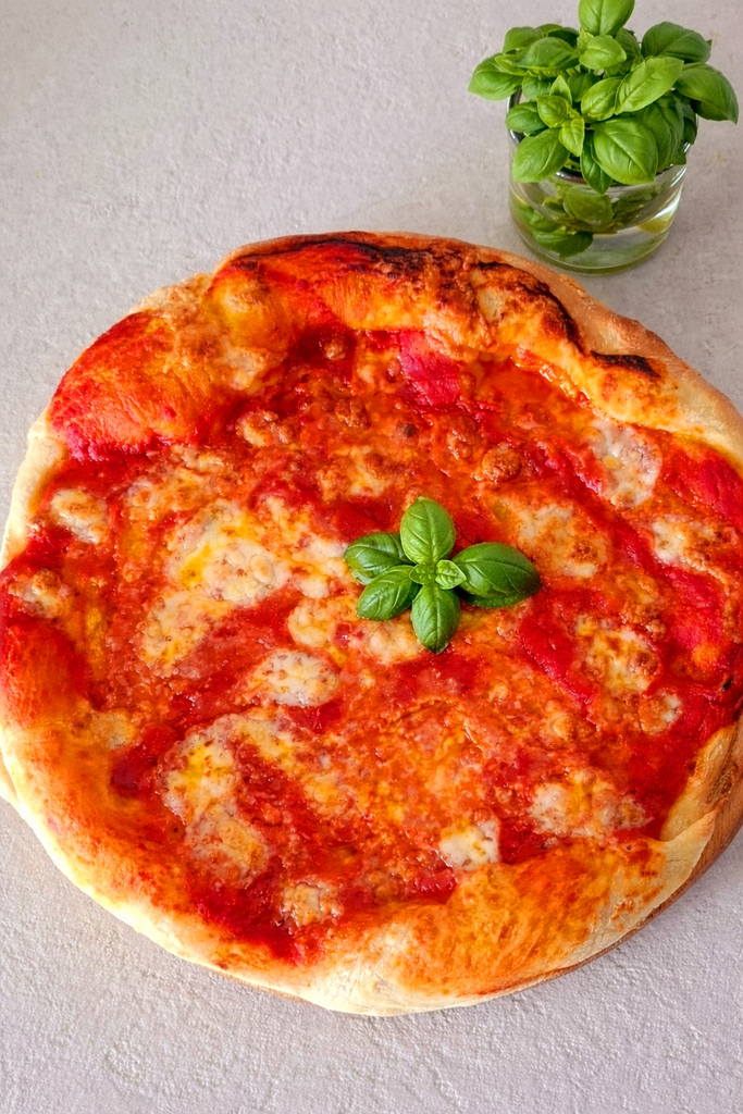 Pizza Margherita servita su tagliere con basilico e vicino vasetto con piantina basilico