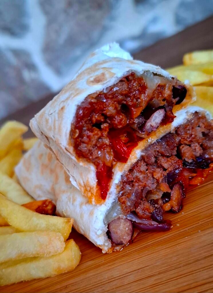 Zoom su ripieno burritos con carne fagioli e peperoni con patatine fritte su tavolo legno e pietra vista come sfondo