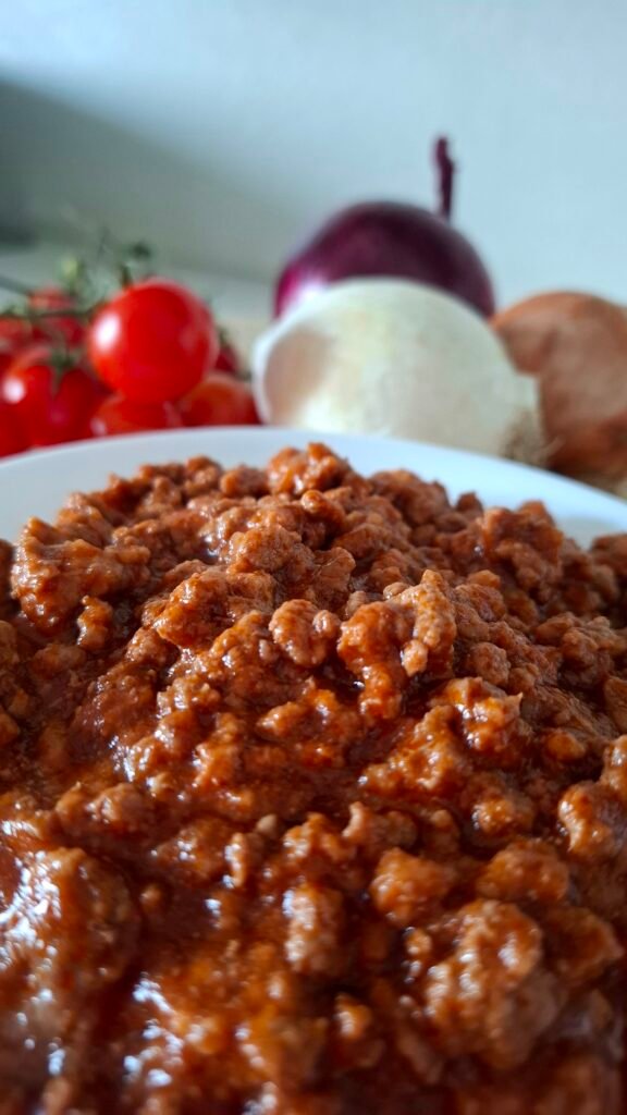 Ragù bolognese con manzo e salsiccia cremoso e veloce presentato in terrina bianca con sfondo di cipolle 