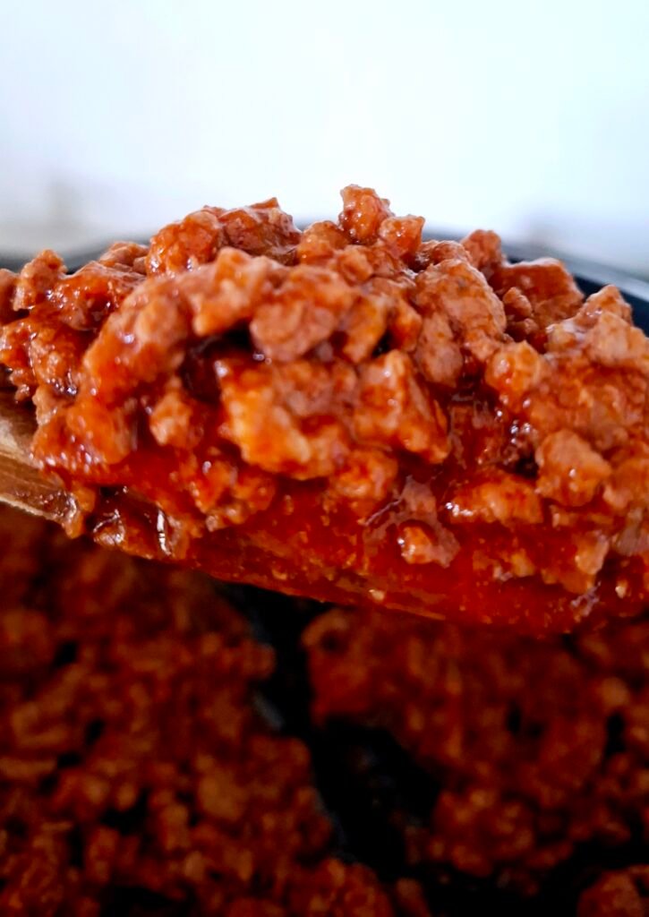 Primo piano sul cucchiaio in legno che contiene un ragù bolognese manzo e salsiccia cremoso e gustoso