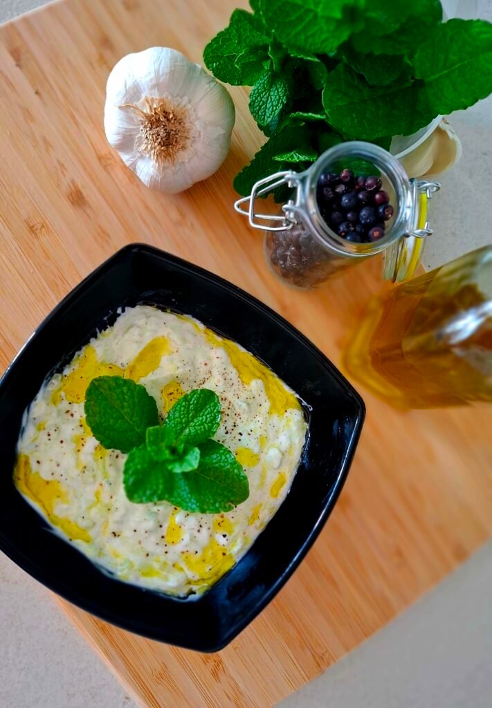 Tzatziki cremosa con menta aglio olio e pepe in ciotola nera su tagliere 