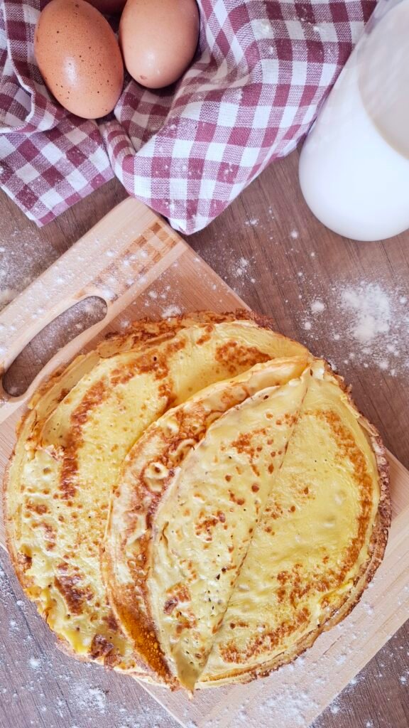 8 Crepes dorate e  maculate servite su tagliere con sfondo di uova latte farina tovaglietta quadri bordeaux e bianca