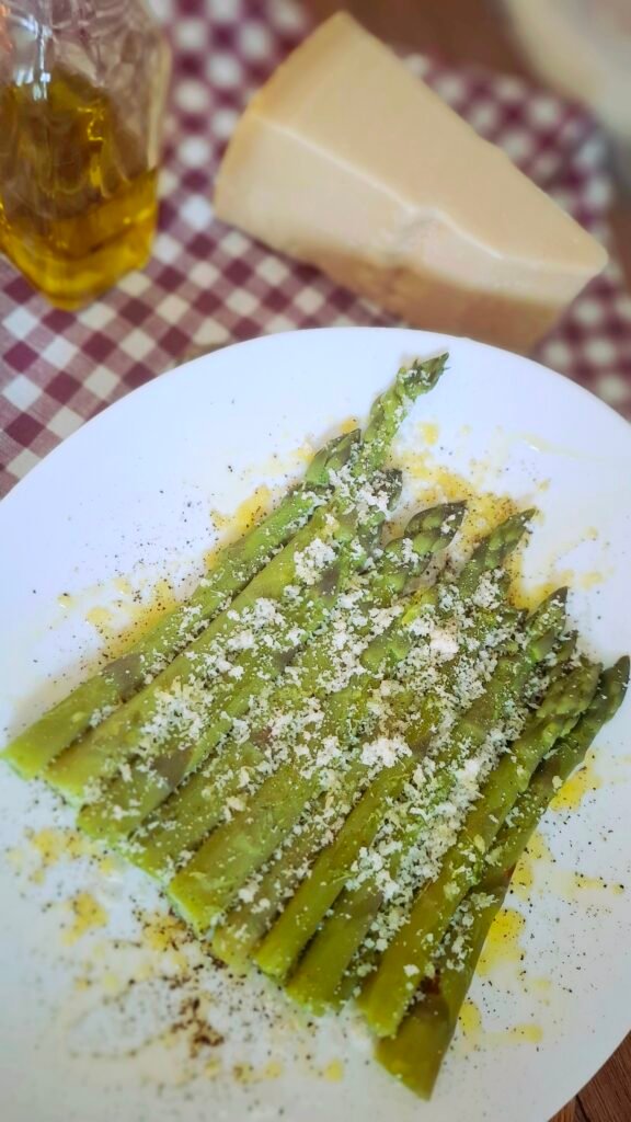 Asparagi bolliti verde brillante su piatto bianco con parmigiano olio e pepe con sfondo di pietra a vista