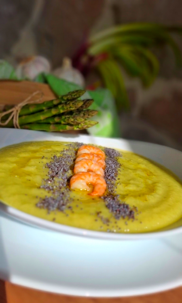 Vellutata cremosa di recupero dei gambi asparagi con code mazzancolla in linea e semi papavero che crea contrasto su tavolo legno e pietra a vista