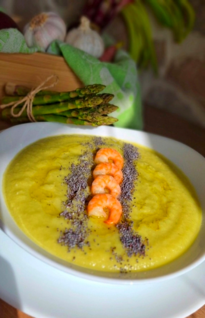 Vellutata cremosa di recupero dei gambi asparagi con code di mazzancolla e semi di papavero su fondina bianca che contrasta con legno e pietra a vista 