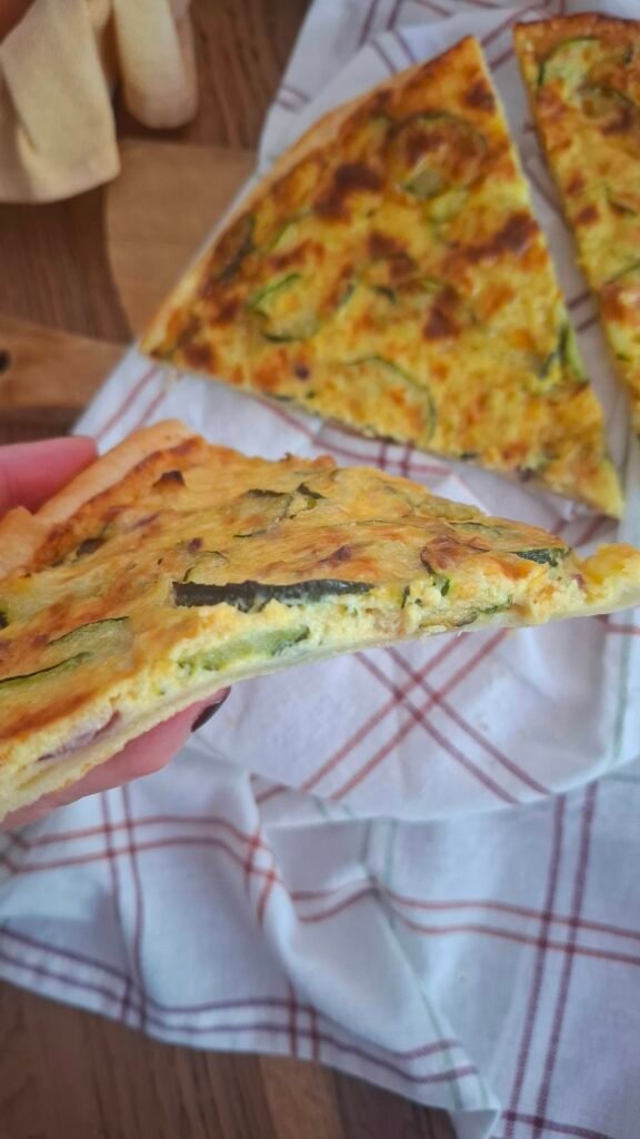 Mano che mostra interno cremoso quiche zucchine e crema cipollotti