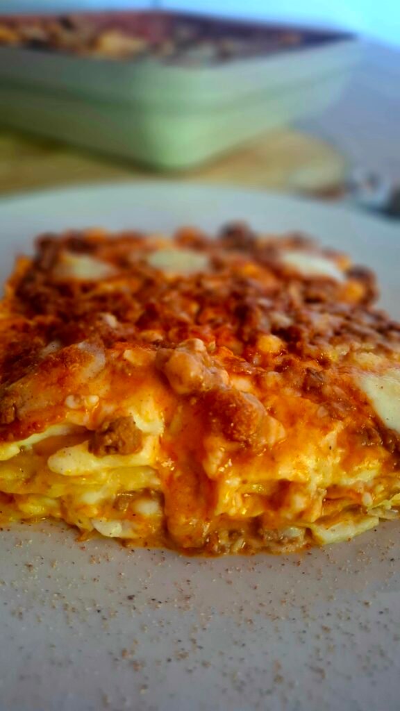Lasagne morbide e succulente filanti su piatto a contrasto con sfondo di pirofila forno