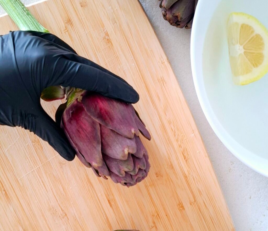 Mano con guanto che afferra carciofi su tagliere 