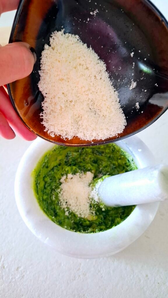 Parmigiano e pecorino versati dalla mia mano nel mortaio sul pesto