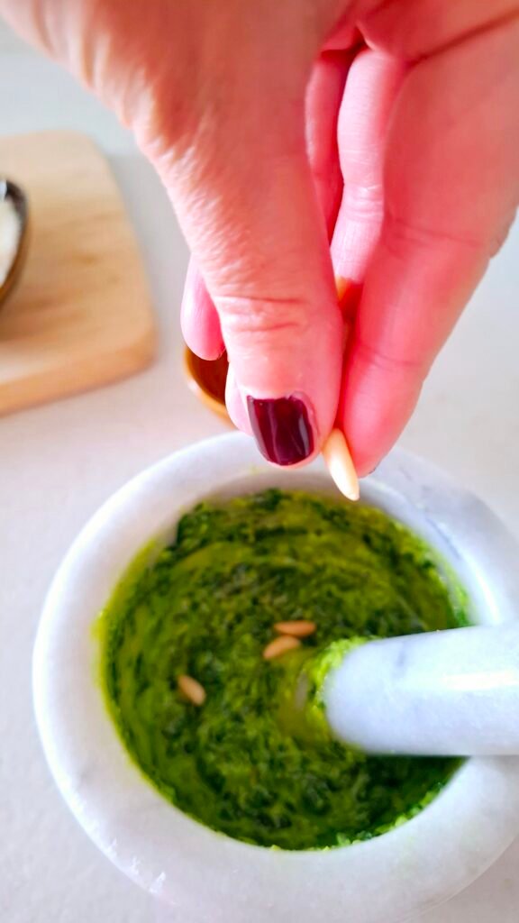 Pinoli che piovono dalla mano nel mortaio sul pesto