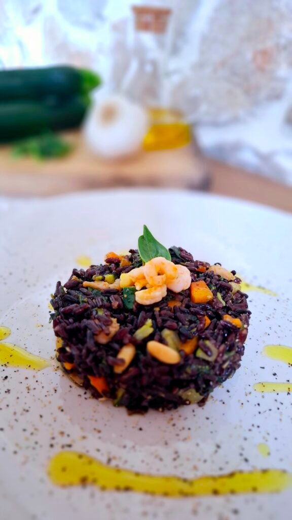 Riso venere nero con gamberetti zucchine carote pesto di basilico su piatto bianco con contrasto del legno