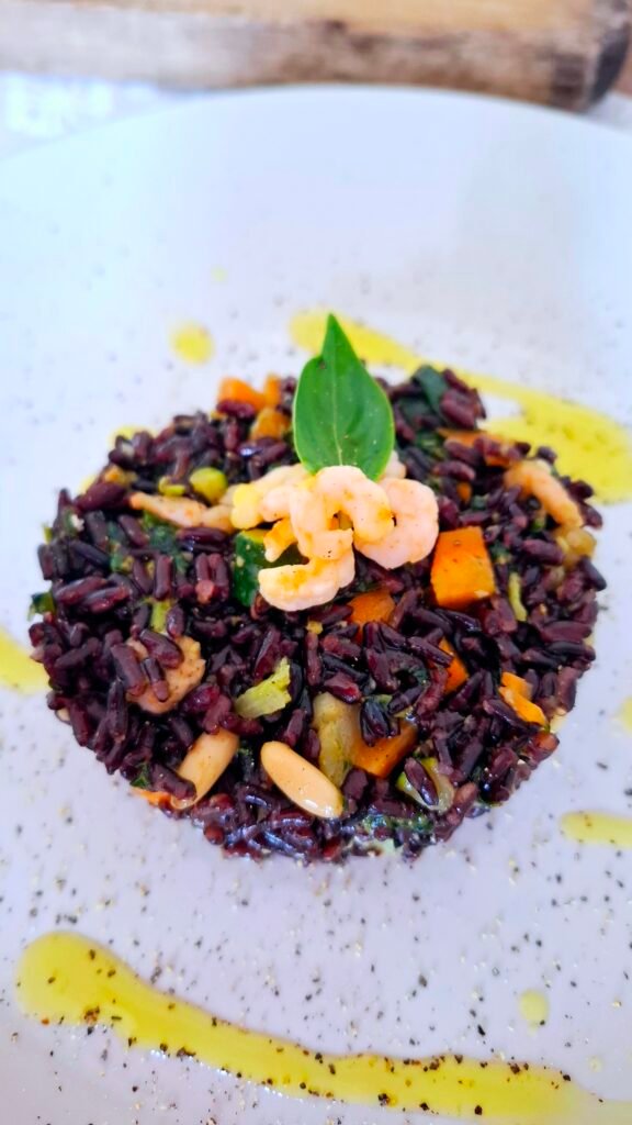 Riso venere con gamberetti carote zucchine pesto su piatto chiaro a contrasto con pepe e olio 