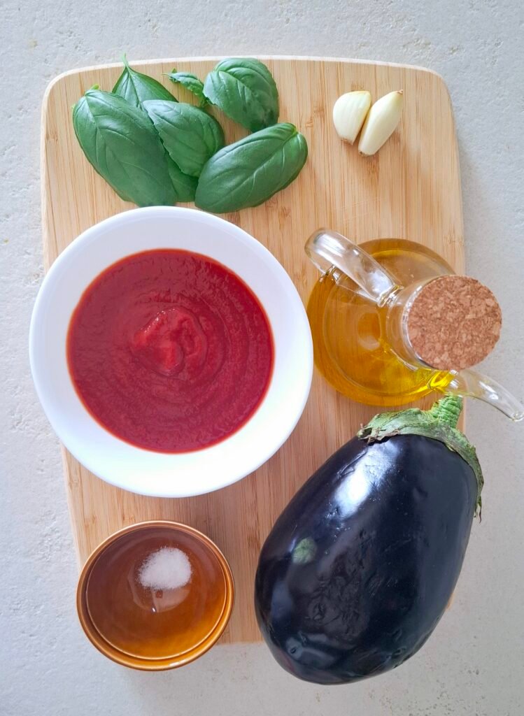 Ingredienti melanzane a funghetto: tagliere con basilico, olio, melanzana, salsa pomodoro e aglio 