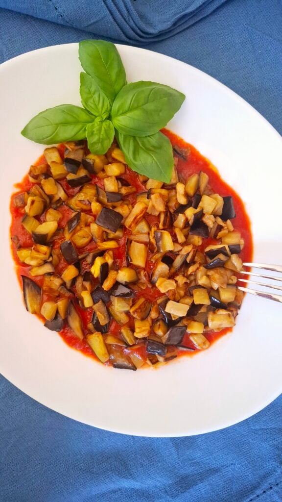 Tovaglia blu a contrasto di piatto bianco con melanzana a funghetto salsa pomodoro all'aglio e basilico