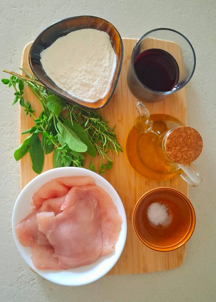 Ingredienti bocconcini pollo al vino rosso: tagliere con petto pollo, vino rosso,farina, erbe aromatiche, olio e sale