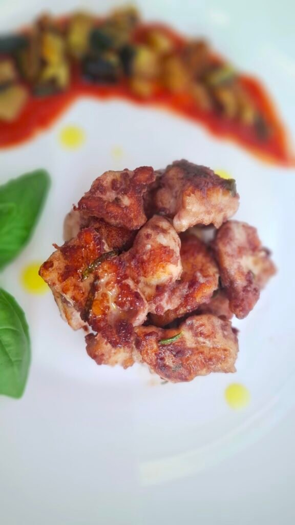 Primo piano di bocconcini al vino rosso croccanti e morbidi con sfondo di melanzane a funghetto su salsa pomodoro e basilico