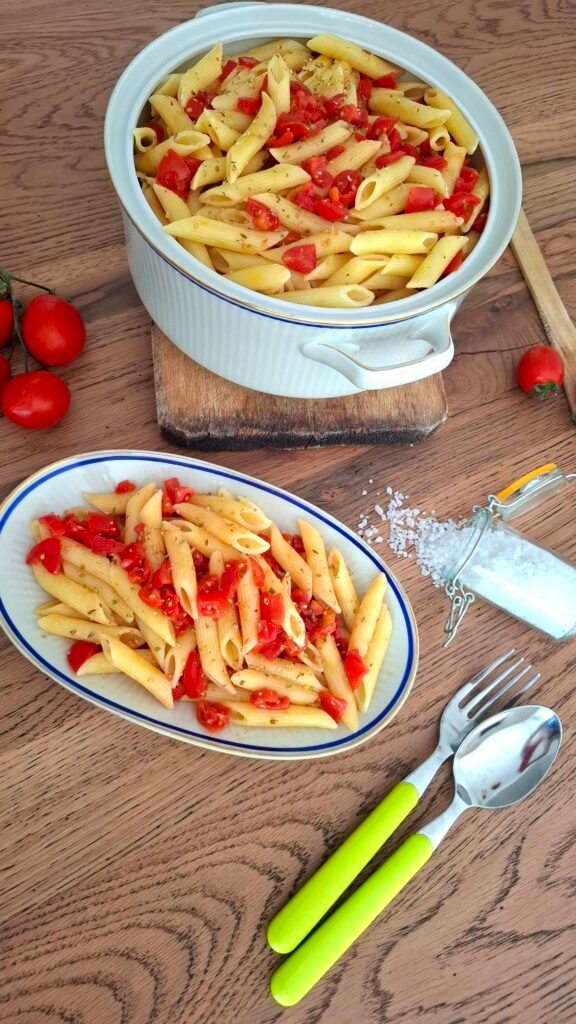 Piattino e terrina con pasta pomodorini origano e aglio su tavolo in legno con posate cucchiaio in legno e pomodorini sparsi con rametto