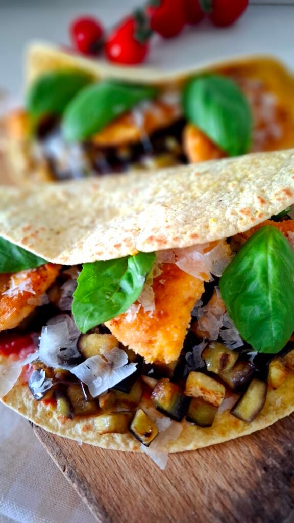 Primo piano sulla farcitura dei tacos con melanzane a cubetti pollo panato scaglie parmigiano salsa pomodoro basilico . Sullo sfondo un altro tacos farcito