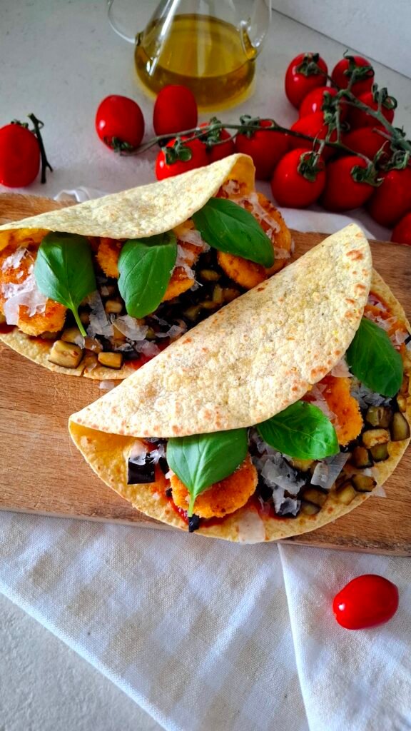 Tagliere in legno con tacos con ripieno abbondante di pollo panato croccante salsa pomodoro piccante melanzane dorate basilico e parmigiano 