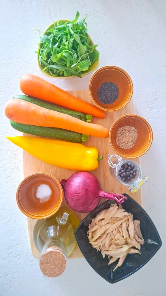 Ingredienti insalata di pollo su tagliere: pollo sfilacciato, Peperone, carote, zucchine, cipolla, semi, pepe, olio e sale