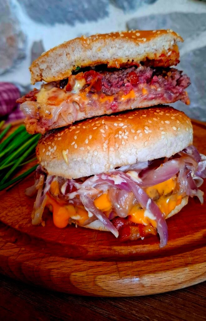 Bacon cheeseburger intero e diviso a metà dove si vede il ripieno succulento con Cipolle dorate, carne di manzo, maionese alla senape miele e erba cipollina
