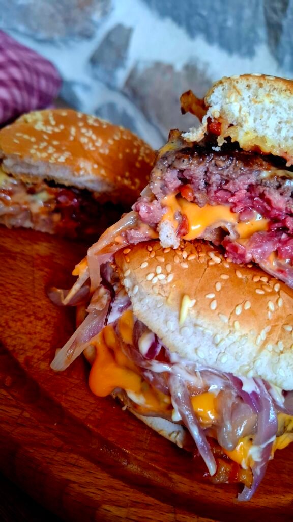 Zoom su interno succulento del bacon cheeseburger con Cipolle dorate, Maionese gourmet con erba cipollina, miele e senape e carne di manzo su tagliere in legno rotondo