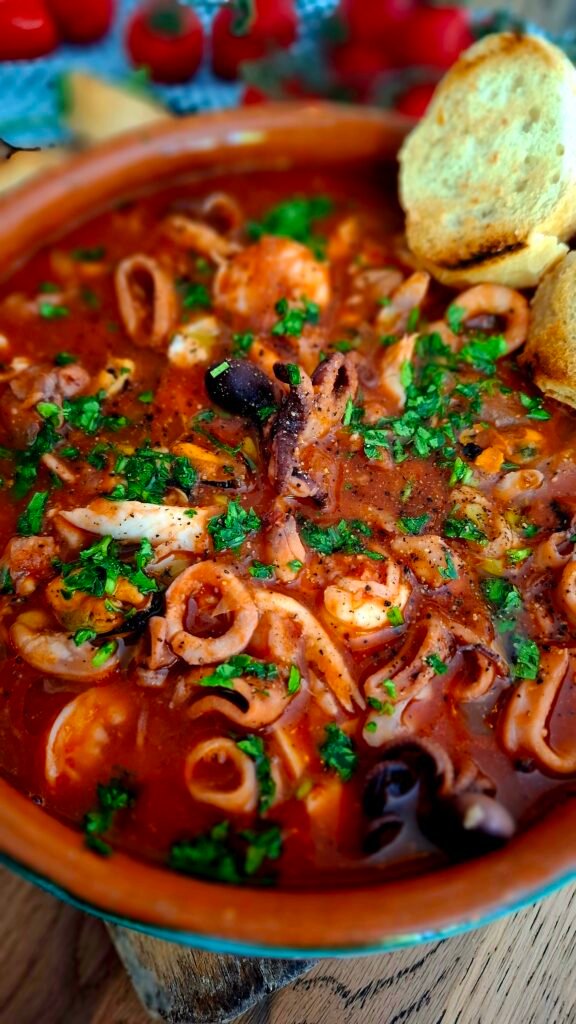 Primo piano sul pesce della zuppa di pesce stile cacciucco a modo mio: piccante, ricca, saporita e veloce .servita in zuppiera di coccio su tagliere in legno