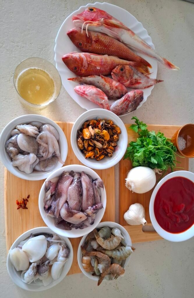 Preparazione ingredienti: calamari, seppie, polipetti, code di mazzancolle, scorfani, gallinella, triglie, cozze sgusciate, passata di pomodoro, vino bianco, olio extravergine d’oliva, prezzemolo fresco, aglio, cipolla, peperoncino, sale grosso, pepe