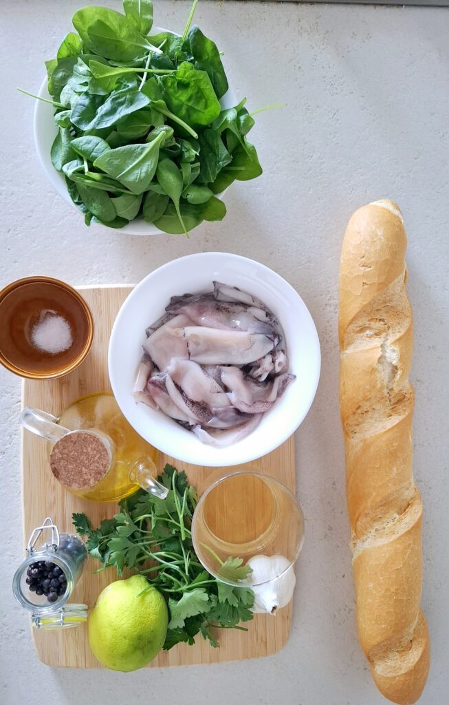 Ingredienti insalata calamari su tagliere:calamari già puliti, spinacini freschi, prezzemolo, vino bianco, aglio, olio extravergine d’oliva, limone, sale fino, pepe nero e pane tipo baguette per le bruschette (facoltativo).
