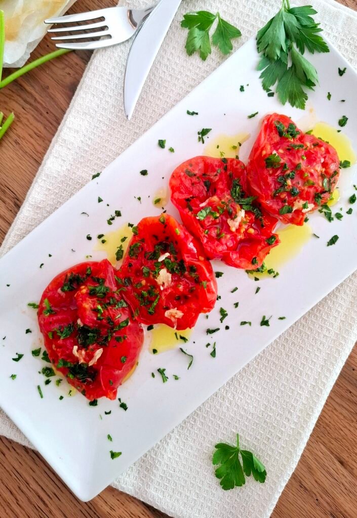 Pomodori in padella con crema di aglio prezzemolo e olio su piatto rettangolare lungo con tovaglietta beige