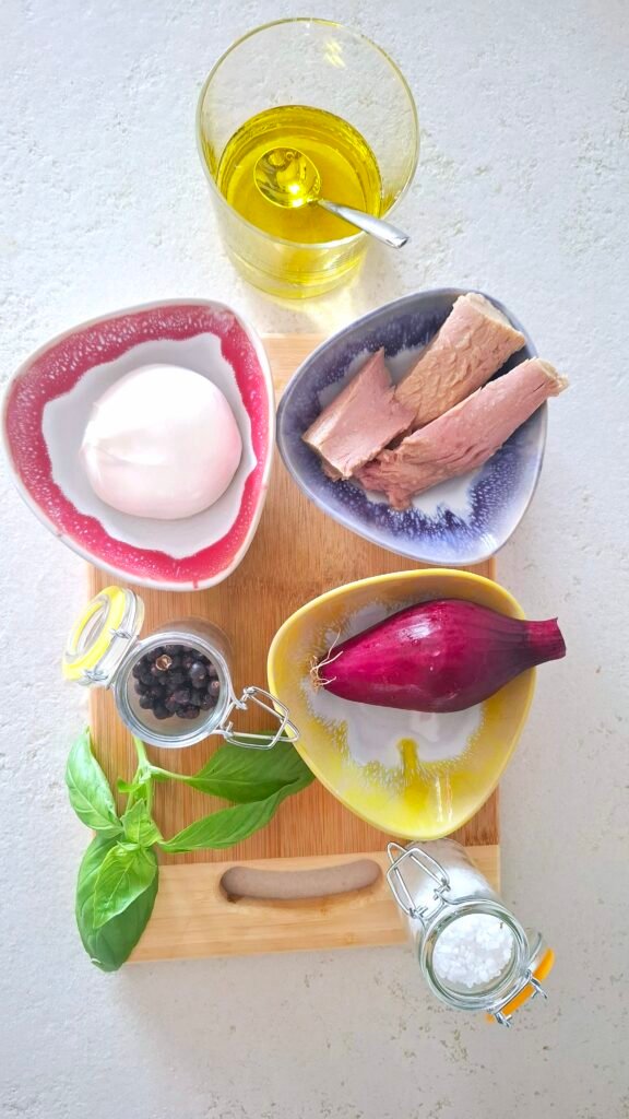 Ingredienti su tagliere: tonno, cipolla, burrata, basilico, sale grosso, pepe nero e emulsione di acqua e olio evo.