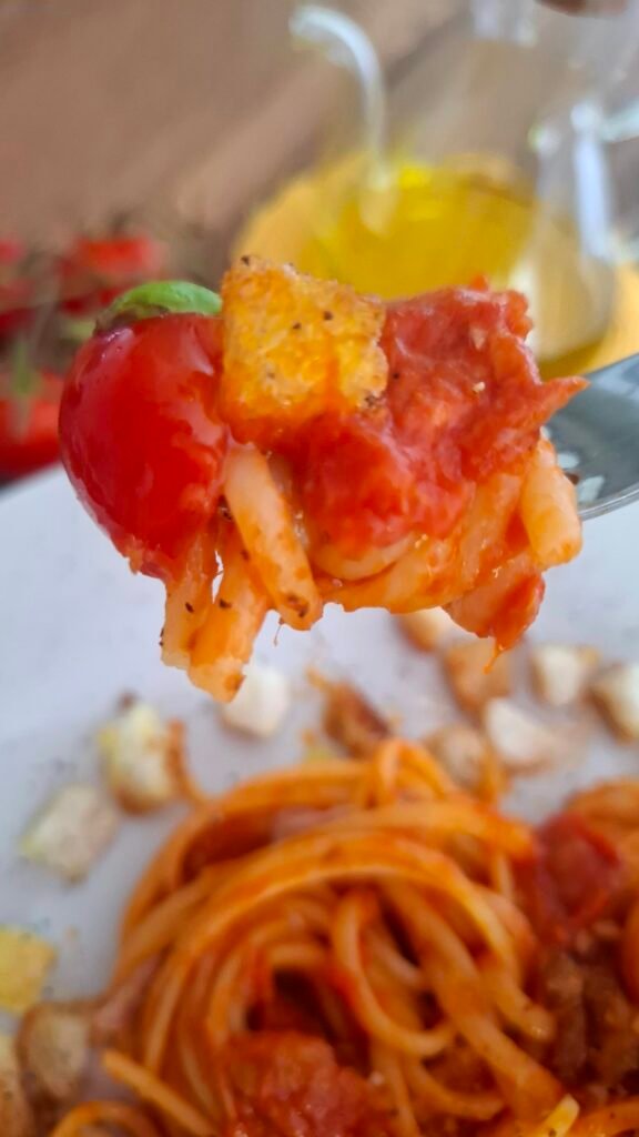 Boccone di linguine al tonno su forchetta .si nota il sugo rosso succulento e cremoso che contrasta con pane croccante