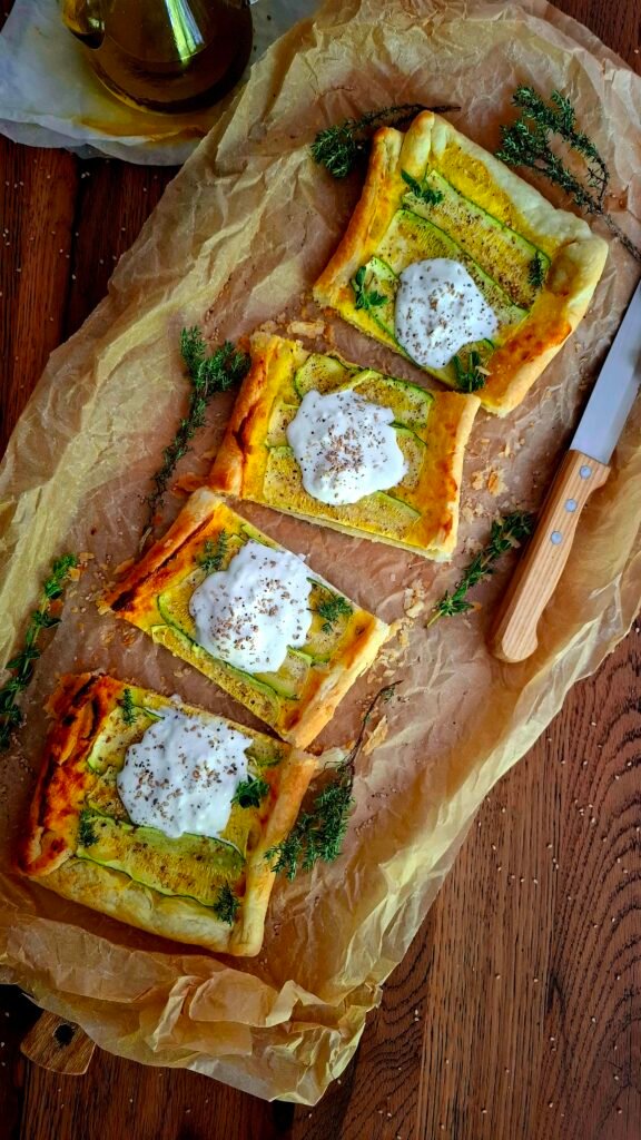 Quiche zucchine e stracciatella tagliata a quadrati sparsi su tavolo legno con erbe aromatiche olio e semi sesamo
