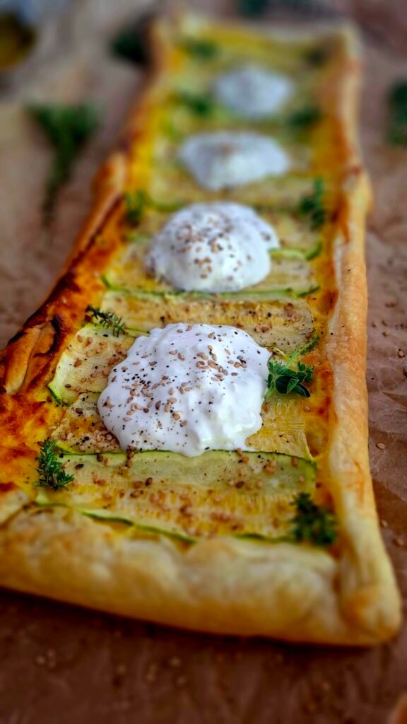 Torta salata zucchine e stracciatella con pepe nero sesamo timo e origano su tagliere legno lungo con carta marrone da forno stropicciato sotto la quiche con erbe aromatiche sparse