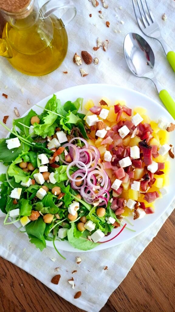 Insalatona su tovaglietta a quadri con posate verde acido e mandorle sparse : misticanza, feta, ceci, speck, patate, cipollotto, mandorle.