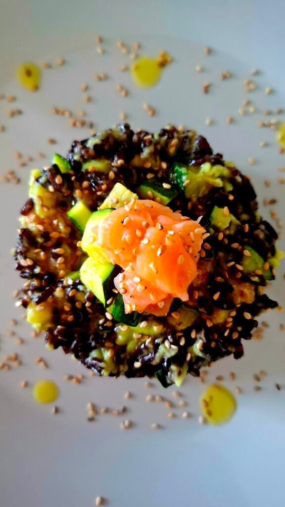 Primo piano su tortino di riso venere con guacamole cremosa zucchine a cubetti e Salmone e semi sesamo tostato