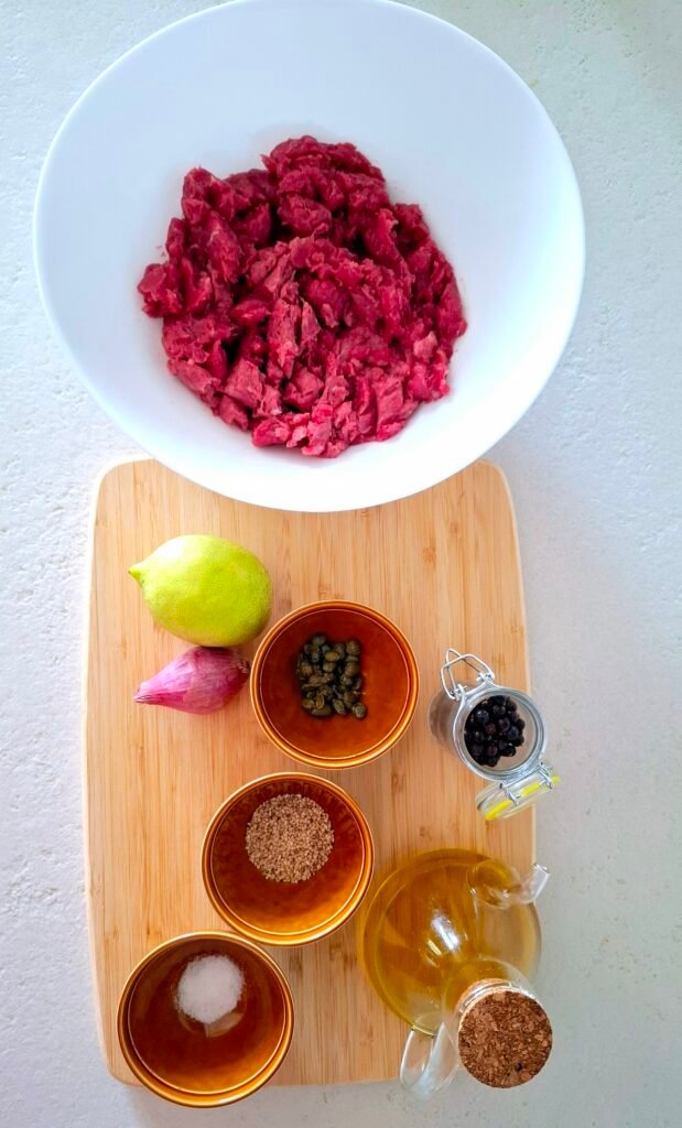 Ingredienti sul tagliere : carne tagliata al coltello, l'olio evo, il limone, il pepe, il sale e lo scalogno, i capperi e i semi di sesamo tostati.