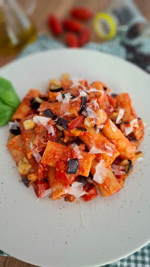 Pasta alla norma cremosa con pecorino basilico melanzane fritte peperoncino e pepe nero su piatto chiaro a contrasto