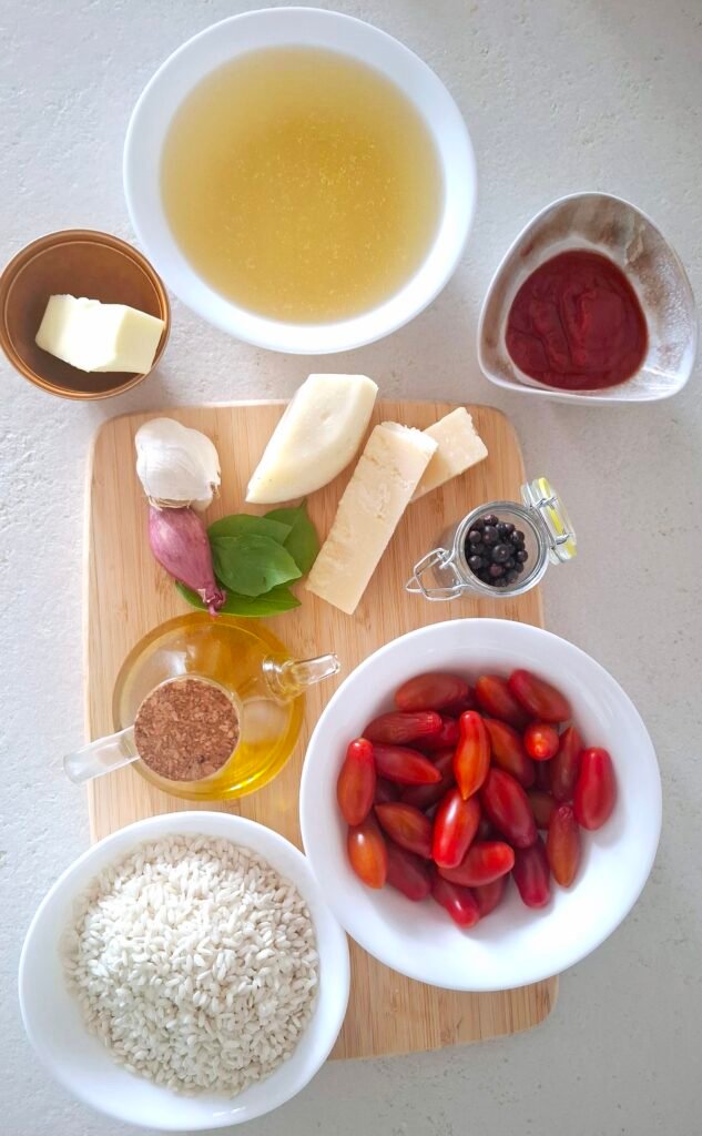 Ingredienti sul piano di lavoro: ​riso, passata di pomodoro, pomodorini, aglio, brodo, caciotta, parmigiano, basilico, pepe, sale, scalogno, burro e olio evo.