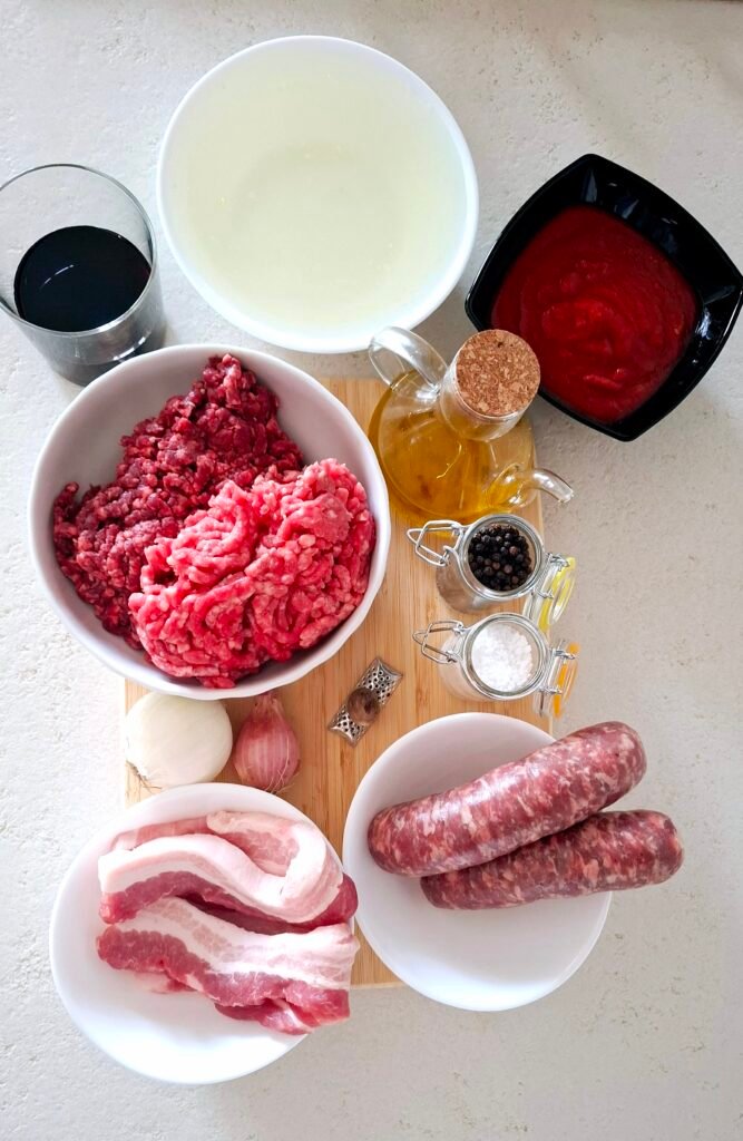 Sul tagliere abbiamo: diaframma, macinato di manzo, salsicce, pancetta, passata di pomodoro, olio evo, noce moscata, pepe, sale grosso, brodo di carne, vino rosso, scalogno, cipolla.