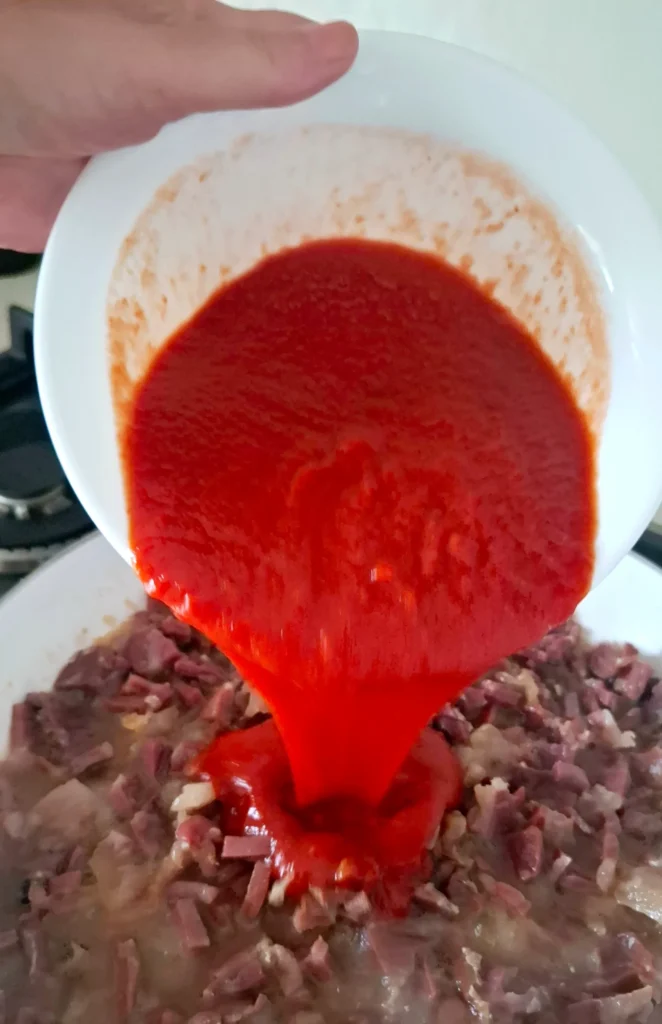 Passata di pomodoro aggiunta a ragù di prosciutto crudo