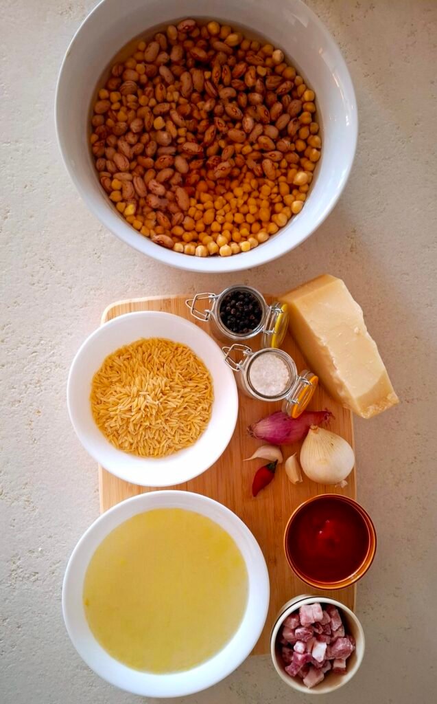 Tagliere in legno con Fagioli, ceci, cicerchie in ammollo, pasta, brodo di cappone, passata di pomodoro, pancetta, cipolla, scalogno, olio, aglio, sale grosso, parmigiano reggiano, pepe e peperoncino