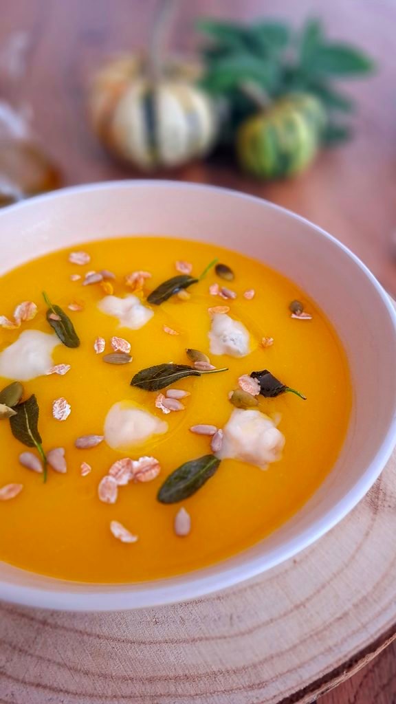 Vellutata cremosa di zucca e patate con salvia fritta gorgonzola e semi, servita in fondina beige su tagliere