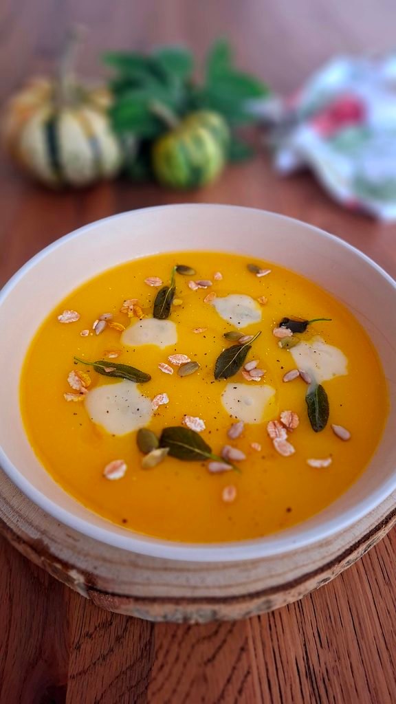 Vellutata zucca e patate con gongorzola, salvia e semi misti tipo girasole e zucca. Sullo sfondo mazzetto di salvia e mini zucche con tovagliolo autunnale