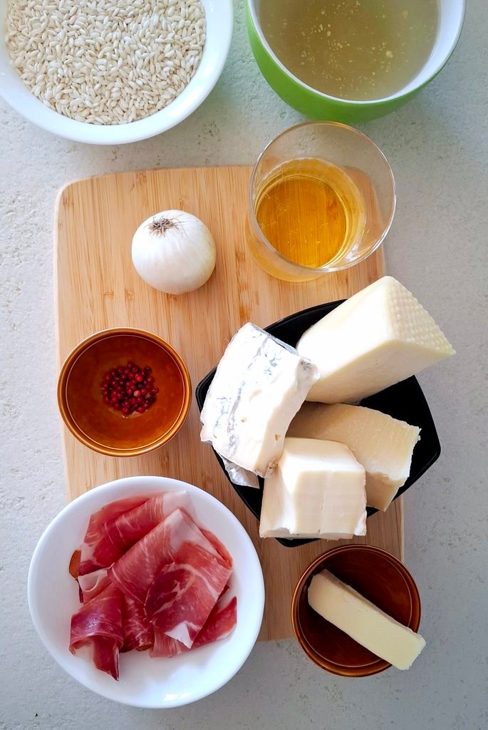 Sul tagliere abbiamo Carnaroli, caciotta, gorgonzola, taleggio, grana padano, brodo di carne, vino bianco, olio extravergine d'oliva, cipolla, pepe rosa e speck.