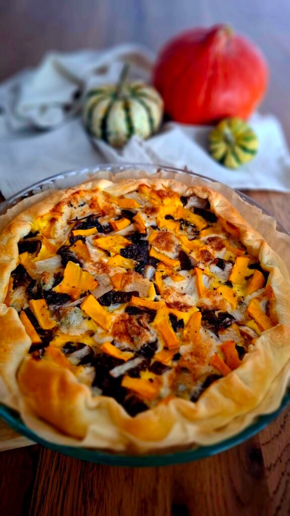 Torta salata autunnale saporita e cremosa con zucca, radicchio trevisano e gorgonzola. Servita in padella in stile rustico con sfondo di 3 zucche di forme e colori diversi.